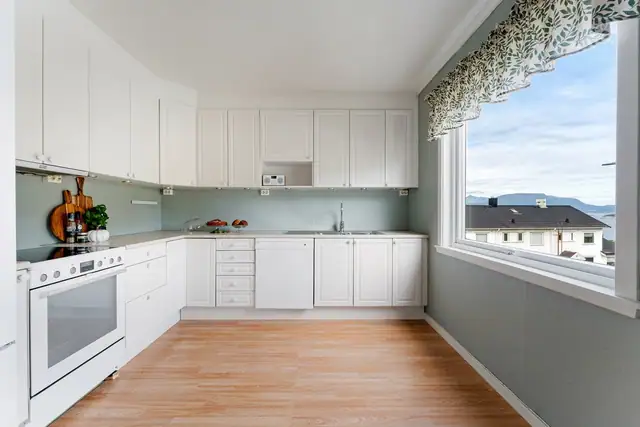 Stort og lyst kjøkken med stor vindusflate som gir rikelig med naturlig lys. Profilerte, malte fronter, laminatbenkeplate og god plass til både oppbevaring og arbeidsflate gjør kjøkkenet praktisk og innbydende.