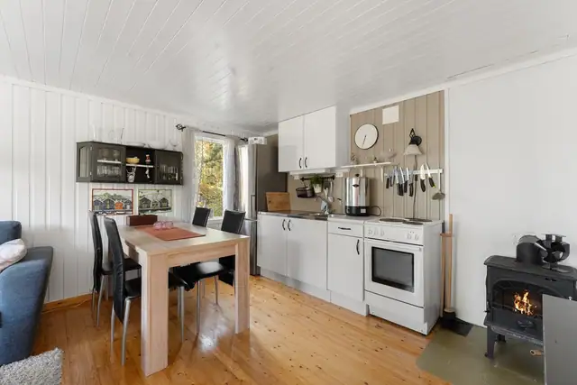 Praktisk kjøkken med glatte fronter, benkeplate i laminat og detaljer i rustfritt stål. Mellom kjøkken og stue er det god plass til spisebord.