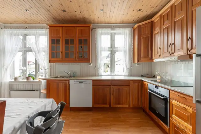 Romslig kjøkken med profilerte fyllingsfronter i varm kirsebærfarget utførelse. Enkelte overskap har glassfelt som gir innredningen et klassisk og elegant uttrykk.