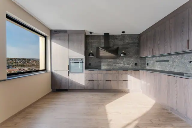 Moderne kjøkkeninnredning med glatte fronter og laminat benkeplate. Kjøkkenet er utstyrt med kjøl/fryseskap, oppvaskmaskin, platetopp og stekeovn, samt kompositt oppvaskkum, vannstoppsystem og komfyrvakt.